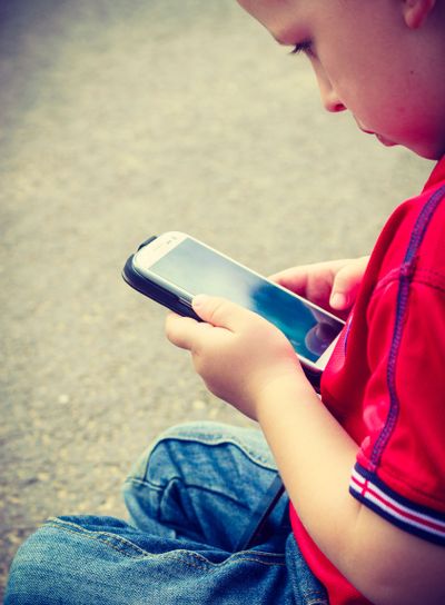 Little boy child playing games on mobile phone outdoor