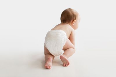 little baby in diaper crawling on white floor