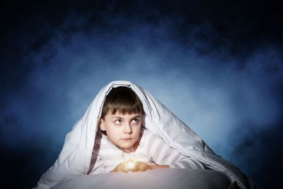 Frightened child hiding under blanket