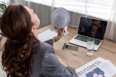 young businesswoman suffering from heat while sitting at...