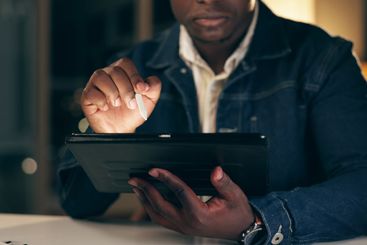 Tablet, black man and working at night in office with...