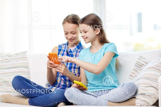 happy girls with smartphones sitting on sofa
