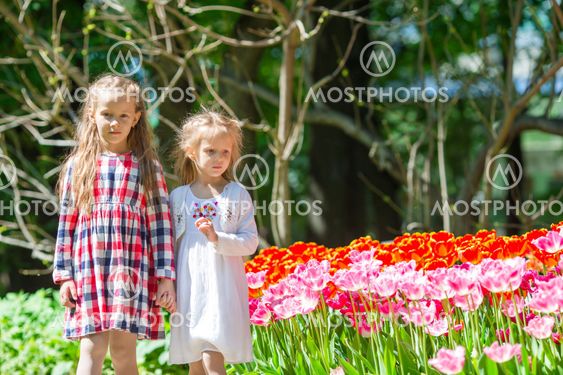 Little adorable girls walking in lush garden of tulips