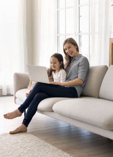Cute little girl using notebook on sofa together with mom