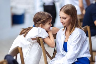 A little girl in a white dress is talking to her sister....