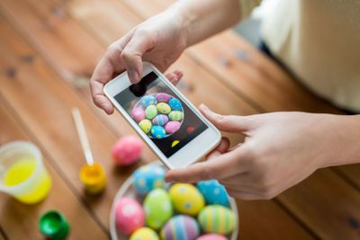 close up of hands with easter eggs and smartphone