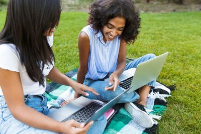 Happy young girls in park using laptop computers on grass.