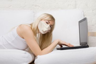 Woman in protective mask using laptop at home