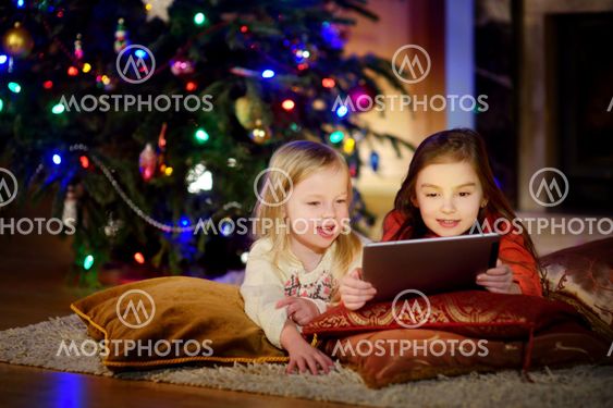 Two cute little sisters using a tablet pc by a fireplace...
