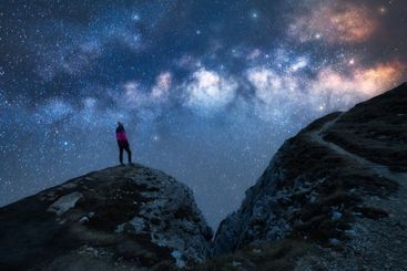 Glowing Milky Way and woman on mountain peak at starry...
