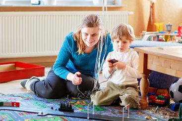 Mother and son playing with racing cars on racetrack,...