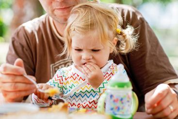 Young middle-aged father feeding cute little toddler...
