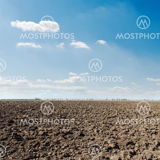 black plowed field and blue sky with clouds