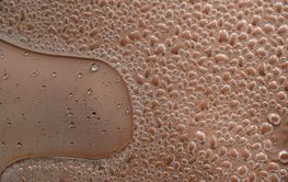 Water droplets forming on brown surface creating textured...