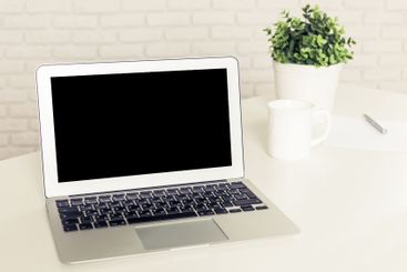 Laptop on a desk with a plant and mug in bright...