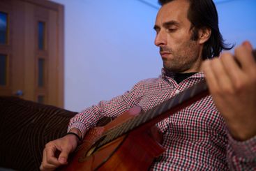 Man thoughtfully strumming an acoustic guitar indoors...