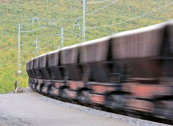 Electrical train with iron ore comes in to a station.