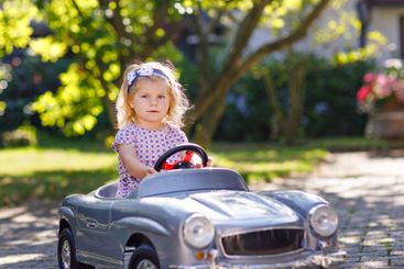 Little adorable toddler girl driving big vintage toy car...