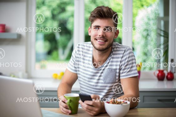 Smiling man using phone while having coffee