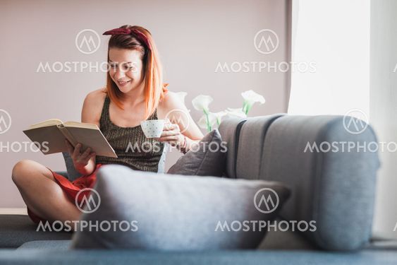Young woman drinking coffee reading book