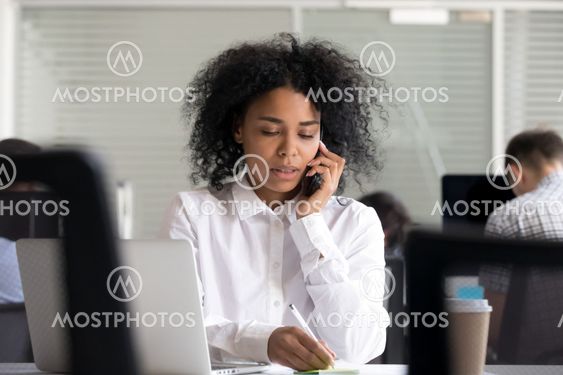 Focused African American woman making notes, talking on phone