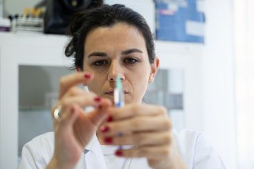 A focused nurse in a white lab coat carefully prepares a...
