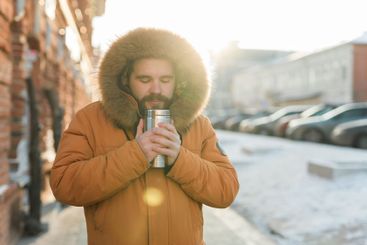 Man enjoying warm drink in sunlight on cold winter urban...