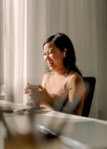 Cheerful businesswoman sitting with coffee cup and laptop...