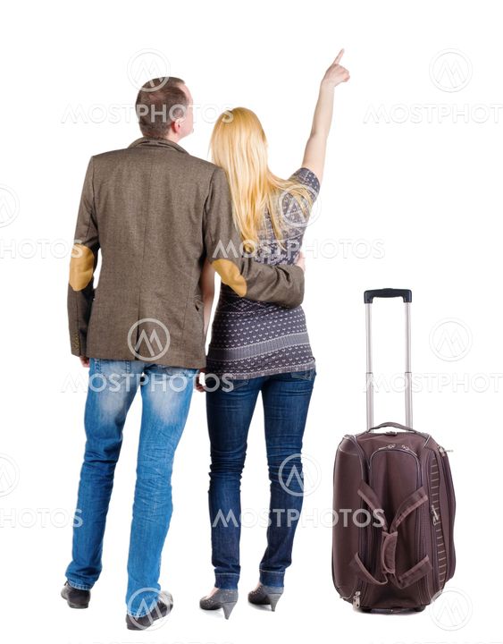 young couple traveling with suitcas and pointing at wal...