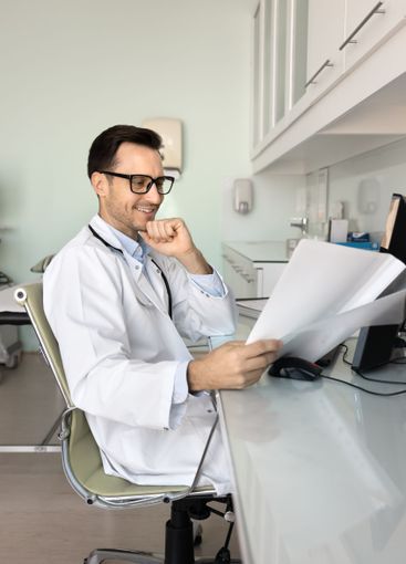 Happy male doctor in glasses reading medical report