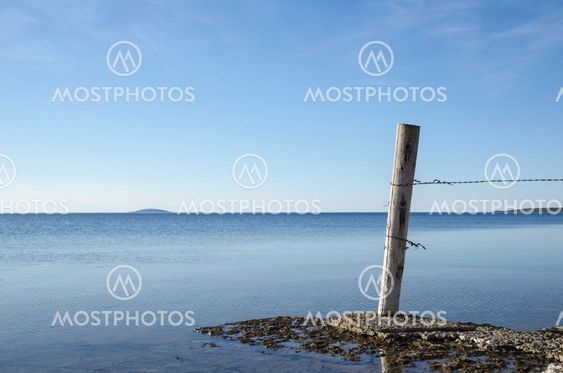 Weathered old wooden pole by a flat rock coast