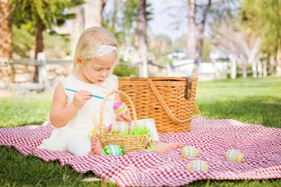 Cute Baby Girl Coloring Easter Eggs on Picnic Blanket