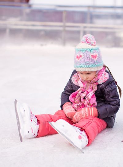 Little sad girl sitting on a skating rink after the fall