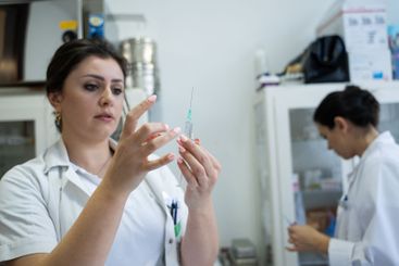 A focused nurse in a white lab coat carefully prepares a...