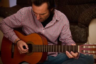 Man playing an acoustic guitar indoors, focused on...