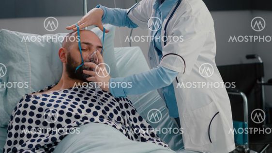 Patient sitting in bed while woman doctor putting oxygen...