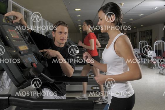 Woman wearing a red t-shirt and black trousers running on a treadmill at gym