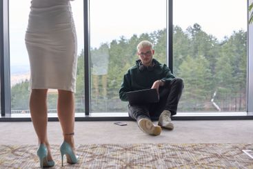 A blonde man sitting casually on the floor of a modern...