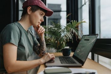 Businesswoman wearing cap working on laptop while sitting...