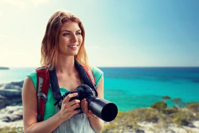 happy woman with backpack and camera over seashore