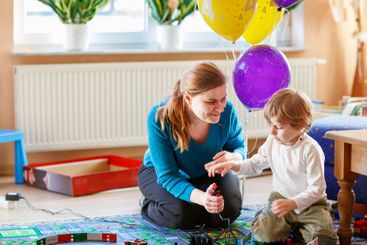 Mother and son playing with racing cars on racetrack,...