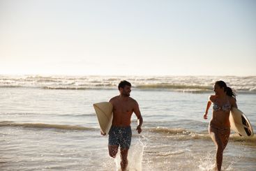 Surfing, couple and running on beach with splash, waves...