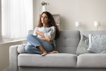 Sad lonely young woman sitting on couch in home interior