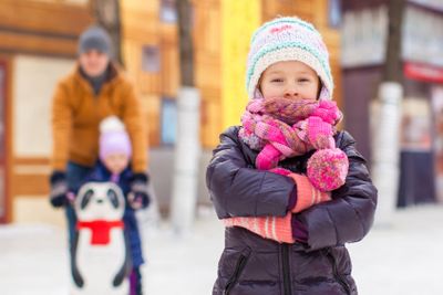 Adorable girl on skating rink, dad with little sister in the background