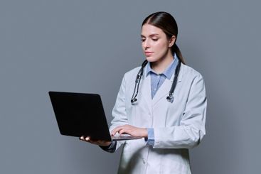 Portrait of serious female doctor using laptop on gray...