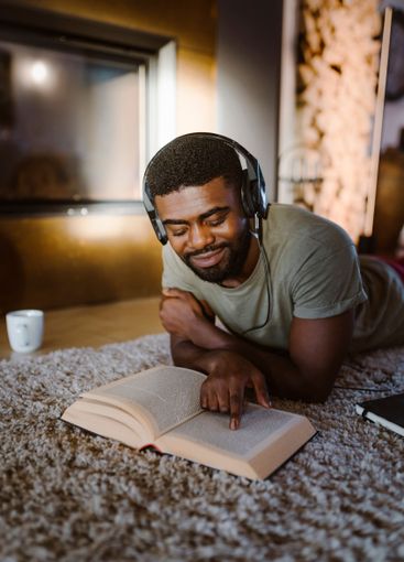 Smiling man reading book while listening to music through...