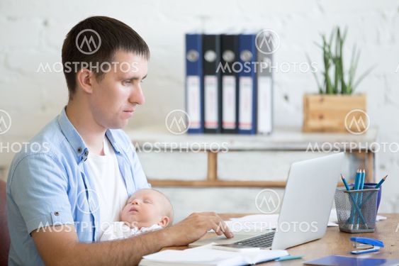 Young father holding newborn child and working on laptop