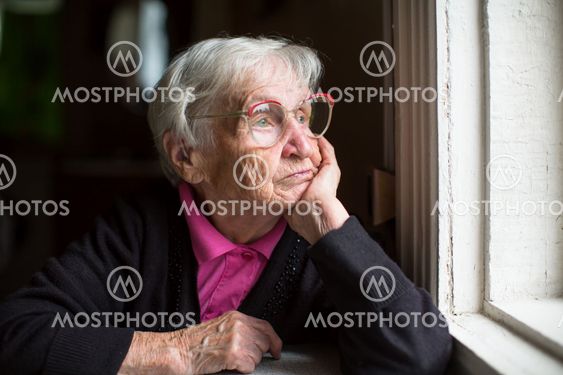 Elderly woman in glasses thoughtfully looking out the window.