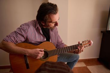 Man playing an acoustic guitar indoors for musical...