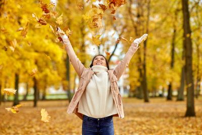 happy woman having fun with leaves in autumn park